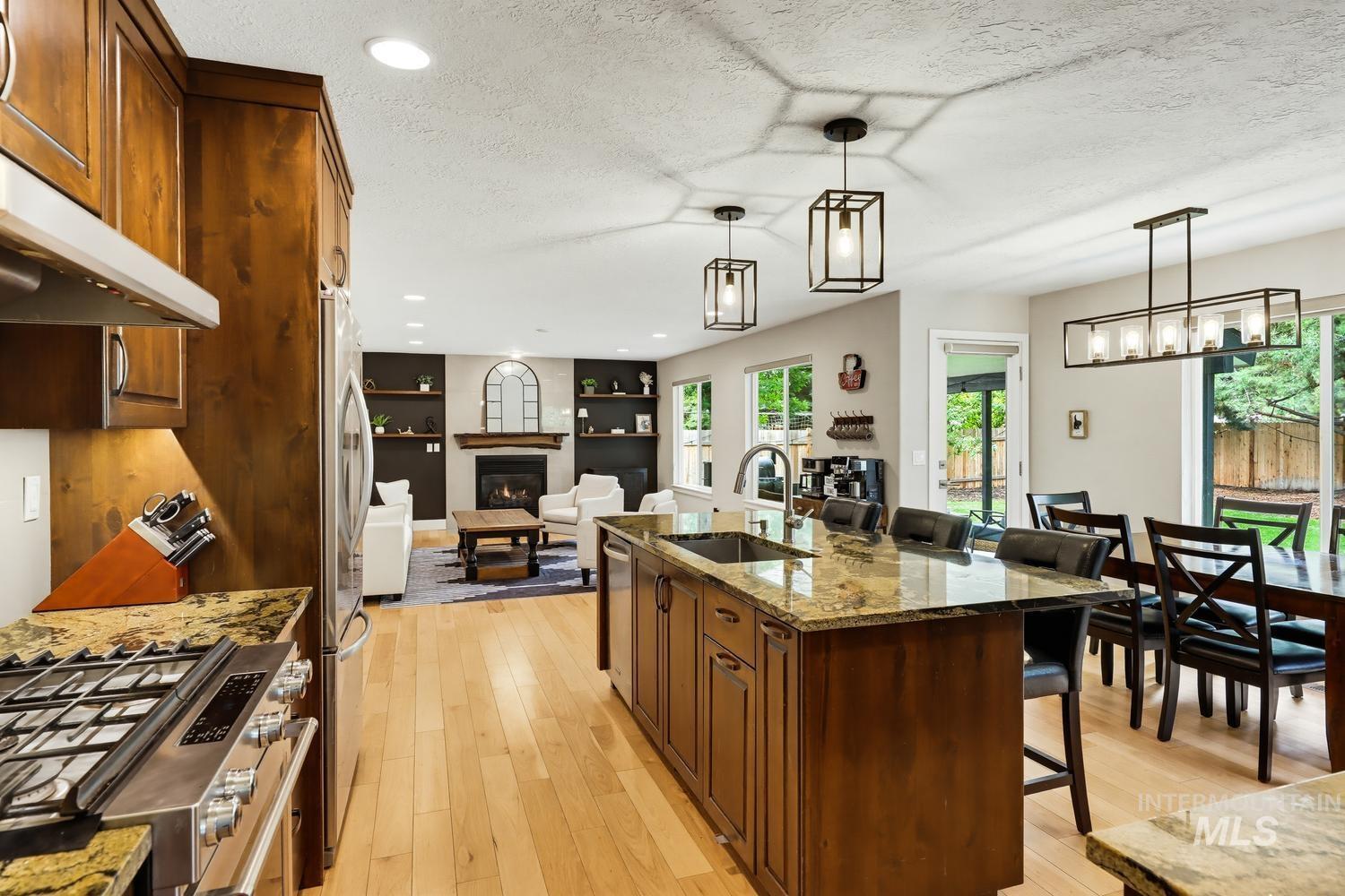 369 South Winthrop Way Boise, ID 83709 - Photo 17 of 50 Open-concept living space featuring wood-finish flooring, a kitchen island with stone countertop, stainless steel appliances, and a fireplace with a mantel