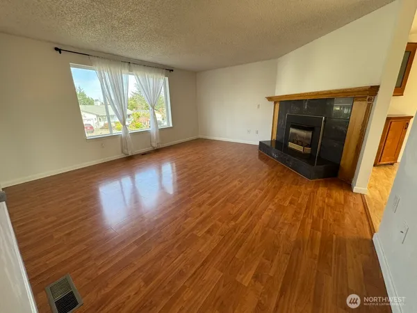 an empty room with wooden floor fireplace and windows