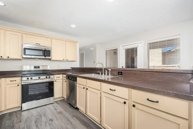 a kitchen with stainless steel appliances granite countertop a sink dishwasher stove and white cabinets with wooden floor