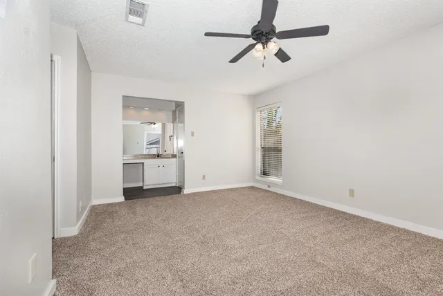 an empty room with a ceiling fan and kitchen view
