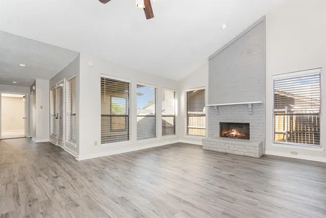 an empty room with wooden floor fireplace and windows