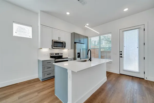 a kitchen with stainless steel appliances a stove top oven a sink a refrigerator with wooden floor and cabinets