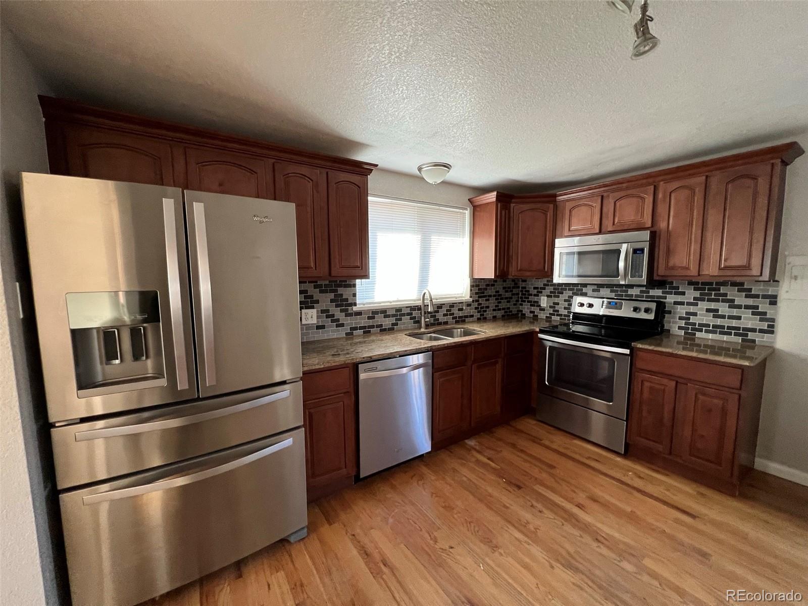 1245 Yates Street Denver, CO 80204 - Photo 4 of 24 a kitchen with granite countertop stainless steel appliances and wooden cabinets