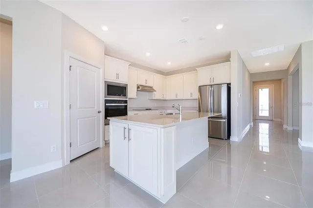 a kitchen with stainless steel appliances a refrigerator a stove top oven a sink and white cabinets