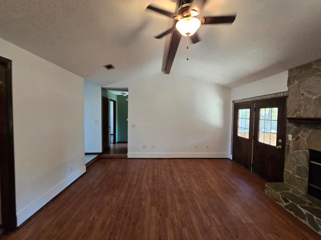 an empty room with wooden floor fan and windows