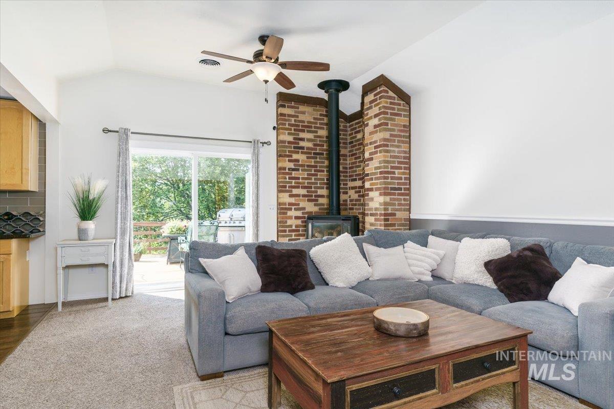 1401 Chokecherry Drive Pocatello, ID 83204 - Photo 10 of 46 Vaulted ceiling living area featuring a prominent brick fireplace with a wood-burning stove, sliding glass doors to the exterior, and a ceiling fan