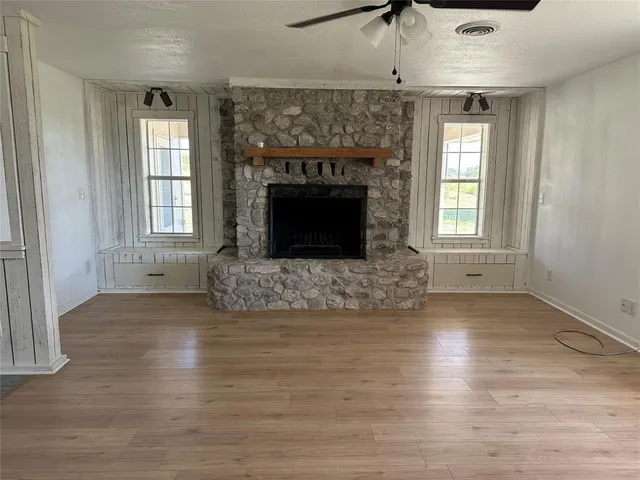 an empty room with wooden floor fireplace and windows