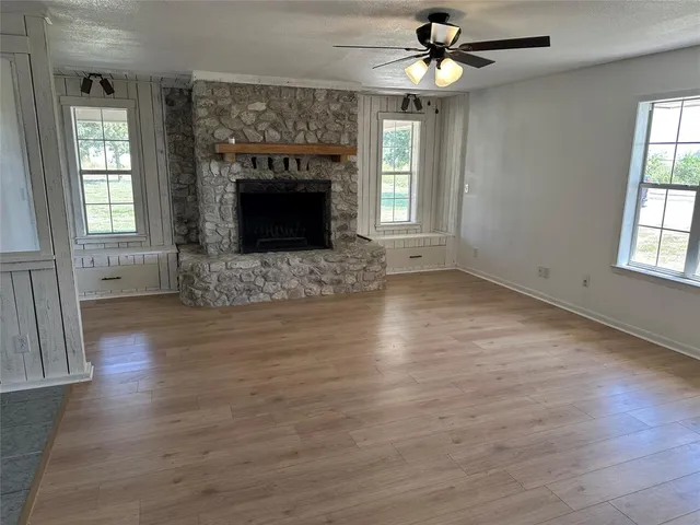an empty room with wooden floor fireplace and windows