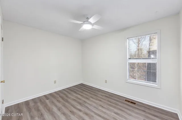 an empty room with wooden floor ceiling fan and windows