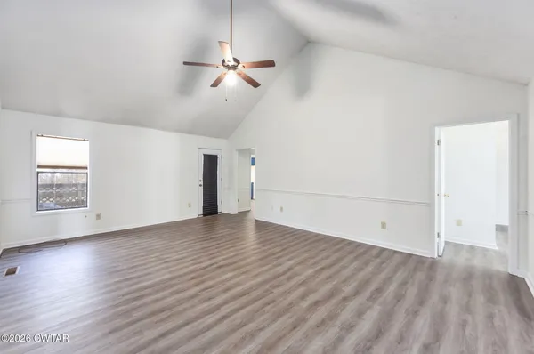an empty room with wooden floor chandelier fan and windows