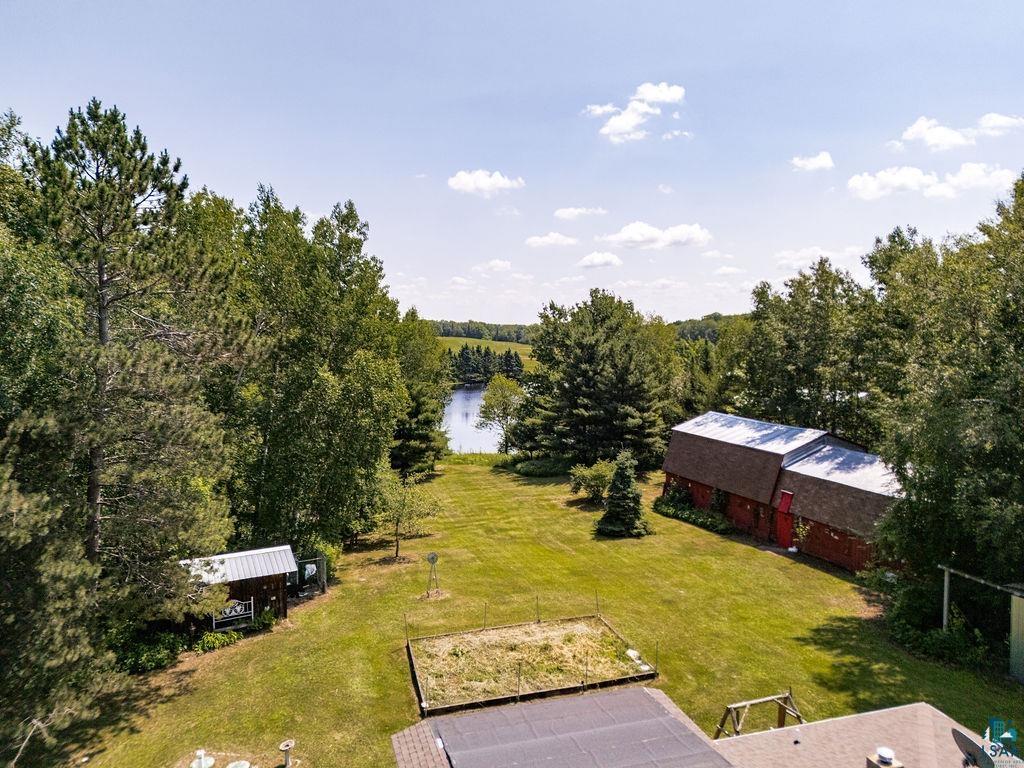 2592 Strandberg Road Barnum, MN 55707 - Photo 37 of 44 Expansive green lawn surrounded by mature trees, a glimpse of a body of water, and a red barn-style outbuilding with a brown roof