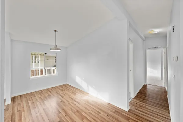 a view of an empty room with wooden floor kitchen and a window