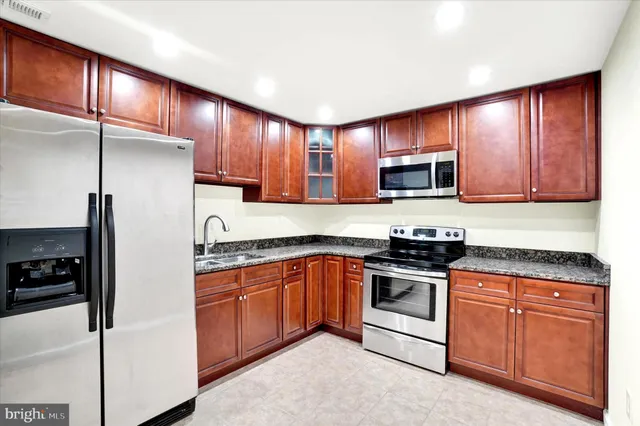 a kitchen with stainless steel appliances granite countertop wooden cabinets a stove a sink and a refrigerator
