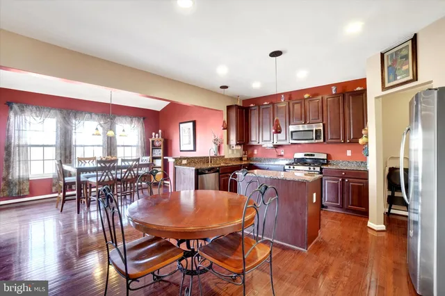 a kitchen with stainless steel appliances granite countertop a stove a refrigerator a kitchen island a dining table and chairs with wooden floor