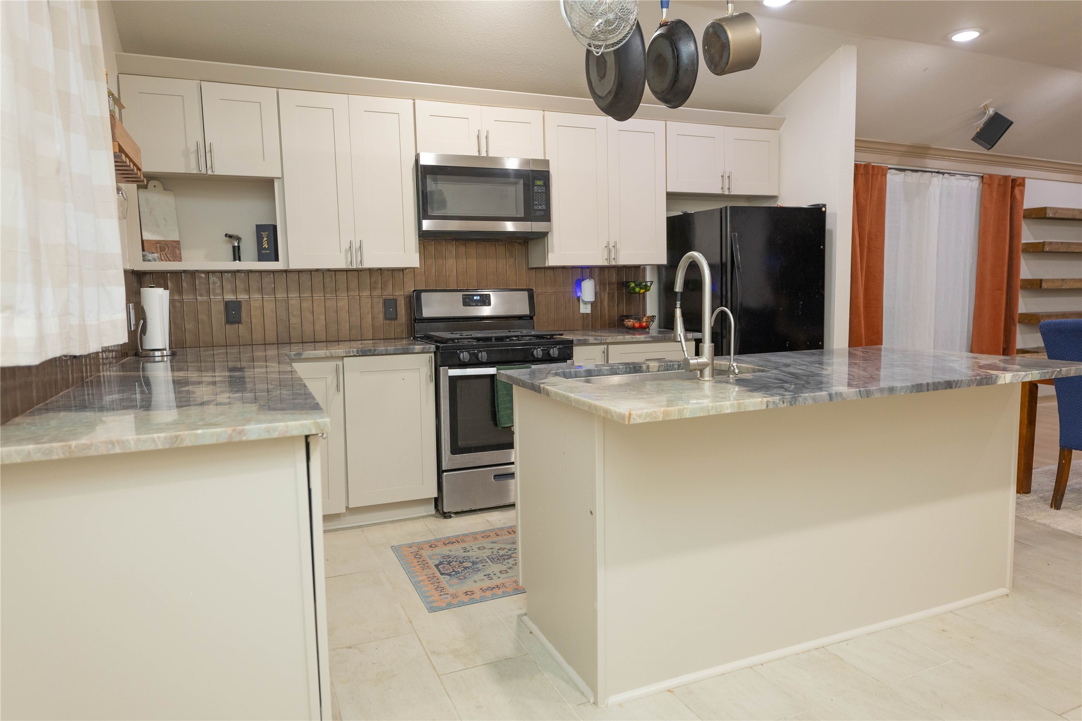 8007 Capitol Street Houston, TX 77012 - Photo 11 of 25 This modern kitchen features sleek white cabinetry, a stainless steel stove and microwave, and a spacious island with a double sink. The neutral backsplash and hanging pot rack add functionality and style.