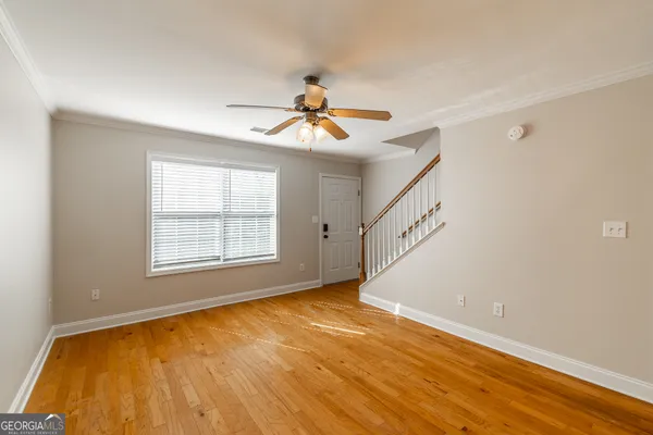 a view of an empty room with chandelier fan and wooden floor