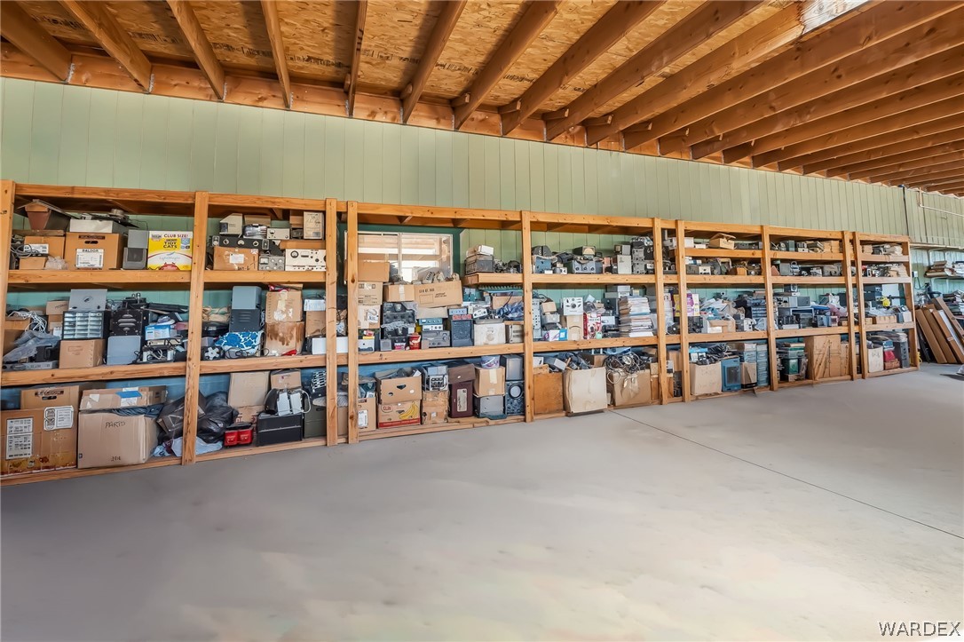 2401 North Stephan Road Kingman, AZ 86401 - Photo 77 of 92 Spacious storage area featuring extensive built-in wooden shelving, a concrete floor, and an exposed wood beam ceiling