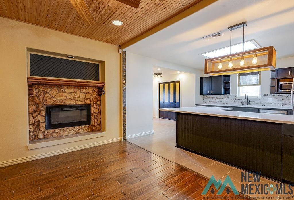 1131 Curry Road North Clovis, NM 88101 - Photo 10 of 69 Open-concept interior featuring wood-finish flooring, a stone-faced fireplace, a kitchen island with a white countertop, dark cabinetry, and a contemporary chandelier