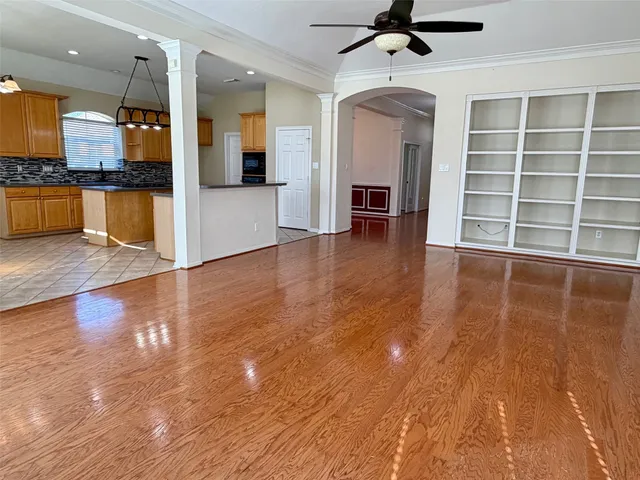 an empty room with wooden floor a kitchen view and windows