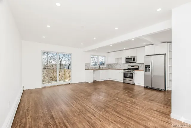 a view of kitchen with stainless steel appliances refrigerator oven and white cabinets with wooden floor