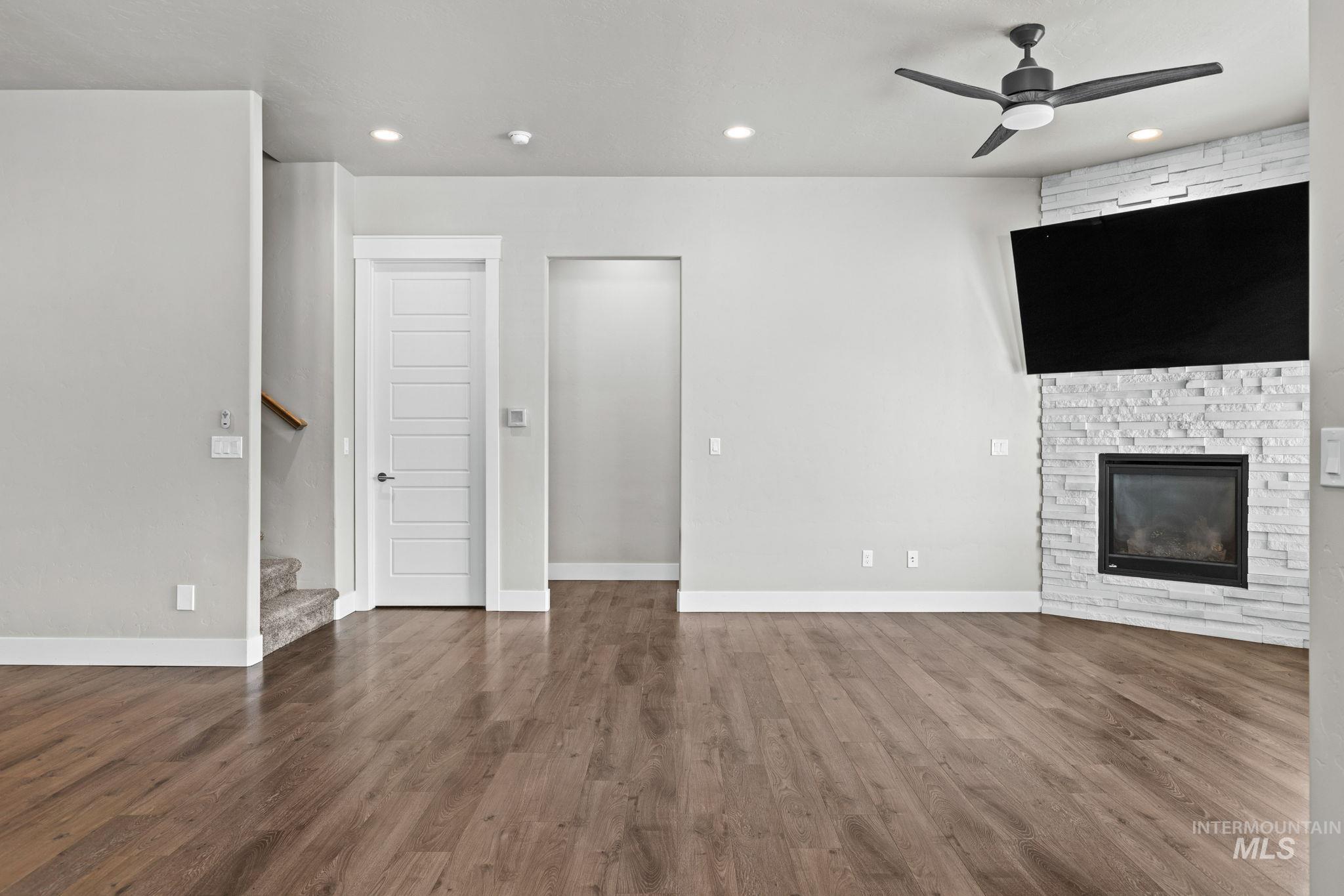 2934 East Murchison Street Meridian, ID 83642 - Photo 17 of 44 Spacious living area featuring wood-finish flooring, a corner fireplace with a stacked stone facade, and a modern ceiling fan