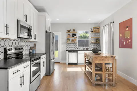 a kitchen with stainless steel appliances a stove a sink dishwasher a refrigerator and white cabinets with wooden floor