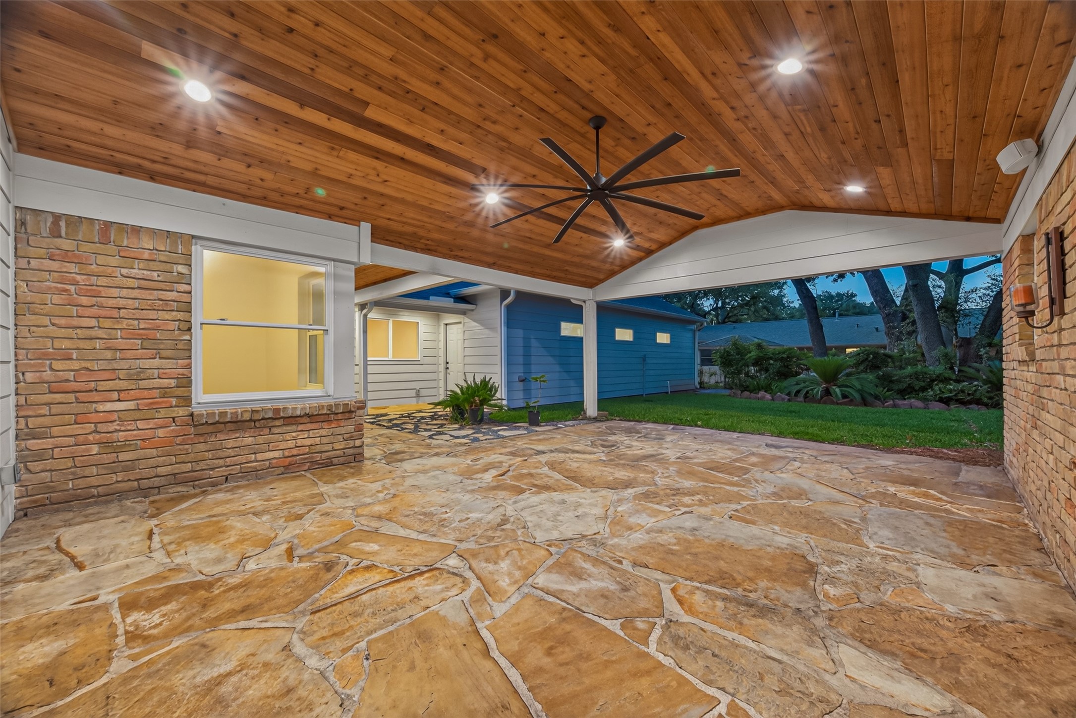 5638 Sanford Road Houston, TX 77096 - Photo 37 of 41 Expansive covered patio showcasing rustic stone floors, a warm wood ceiling with recessed lighting, and a large ceiling fan. Opens directly to a lush backyard, perfect for outdoor living and entertaining.