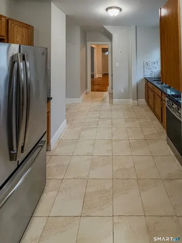 a view of a refrigerator in kitchen and an empty room in wooden floor