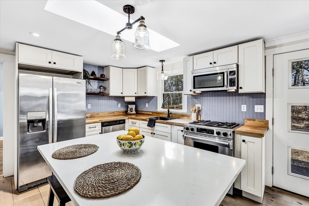 55 Howes Road Wellfleet, MA 02667 - Photo 9 of 33 a kitchen with stainless steel appliances granite countertop a stove a refrigerator a microwave a sink a dining table and chairs with wooden floor