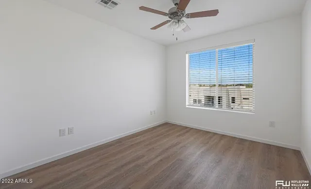 an empty room with wooden floor fan and windows