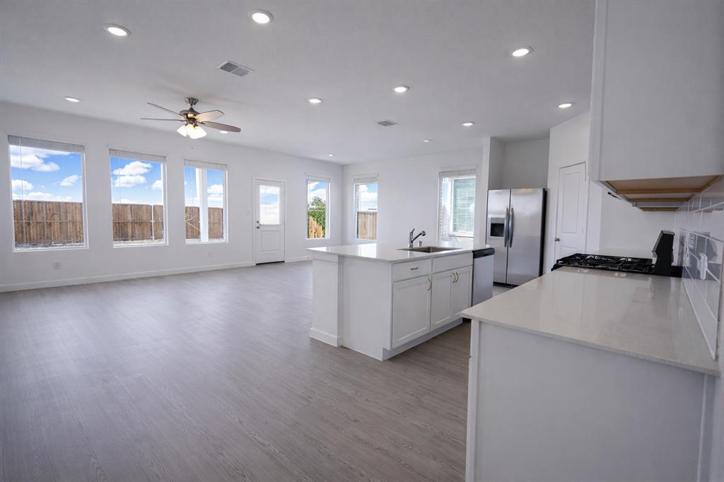 3017 Dutch Road Providence Village, TX 76227 - Photo 29 of 32 Kitchen with a kitchen island with sink, stainless steel appliances, light stone counters, light wood-type flooring, and open floor plan