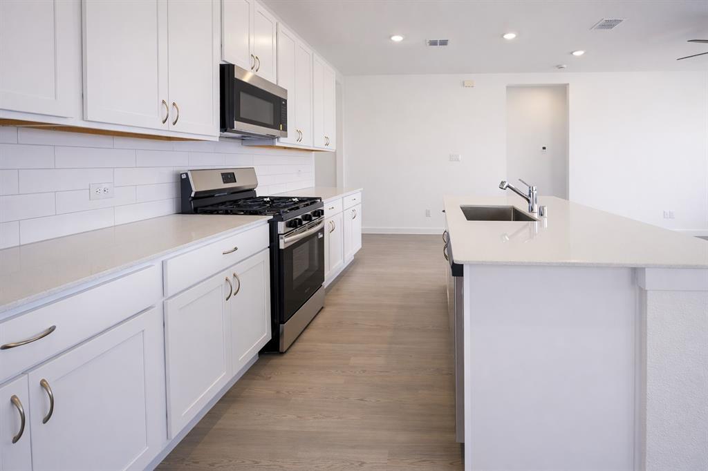 3017 Dutch Road Providence Village, TX 76227 - Photo 8 of 32 Kitchen with stainless steel appliances, white cabinetry, a center island with sink, light wood-style flooring, and light stone countertops