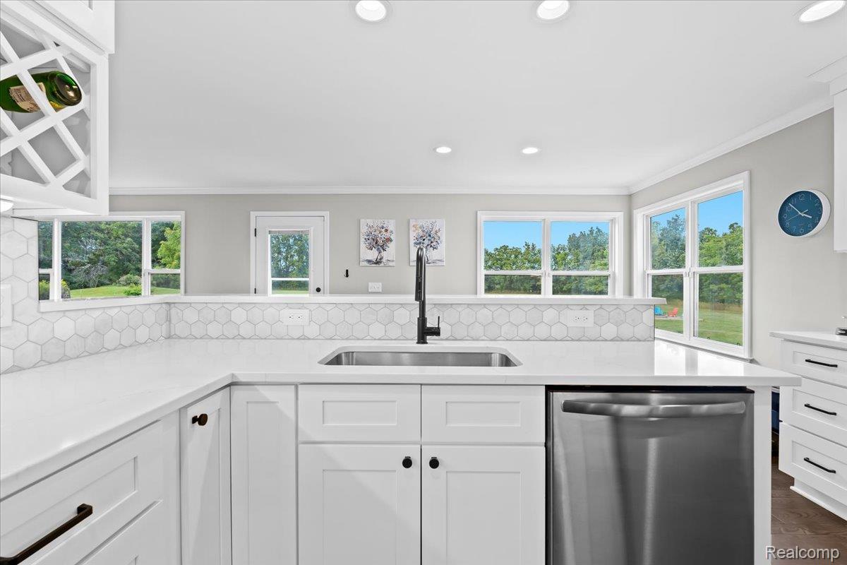 3778 Warner Road Howell, MI 48855 - Photo 10 of 38 Kitchen featuring stainless steel dishwasher, decorative backsplash, white cabinets, light stone counters, and ornamental molding