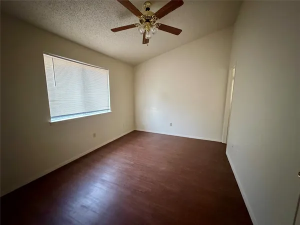 an empty room with wooden floor fan and windows