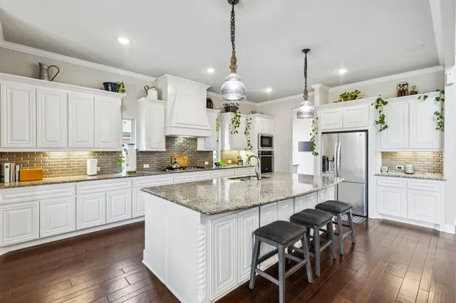a large kitchen with granite countertop lots of white cabinets appliances and furniture