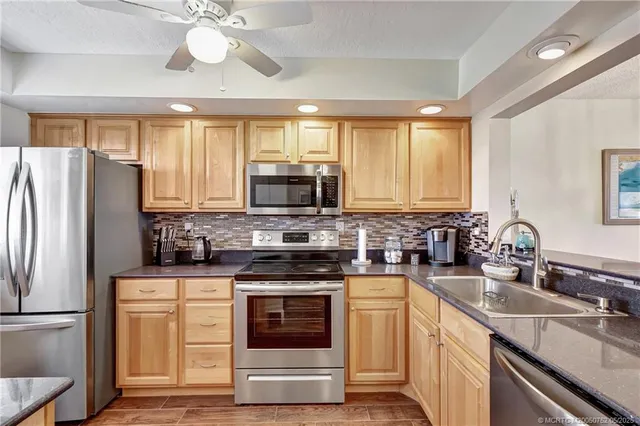 a kitchen with stainless steel appliances granite countertop a sink a stove a refrigerator cabinets and a center island
