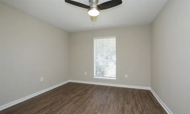 an empty room with wooden floor fan and windows
