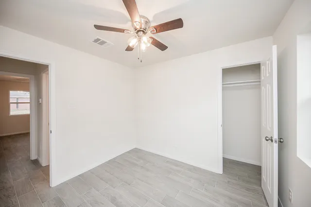 an empty room with wooden floor fan and windows