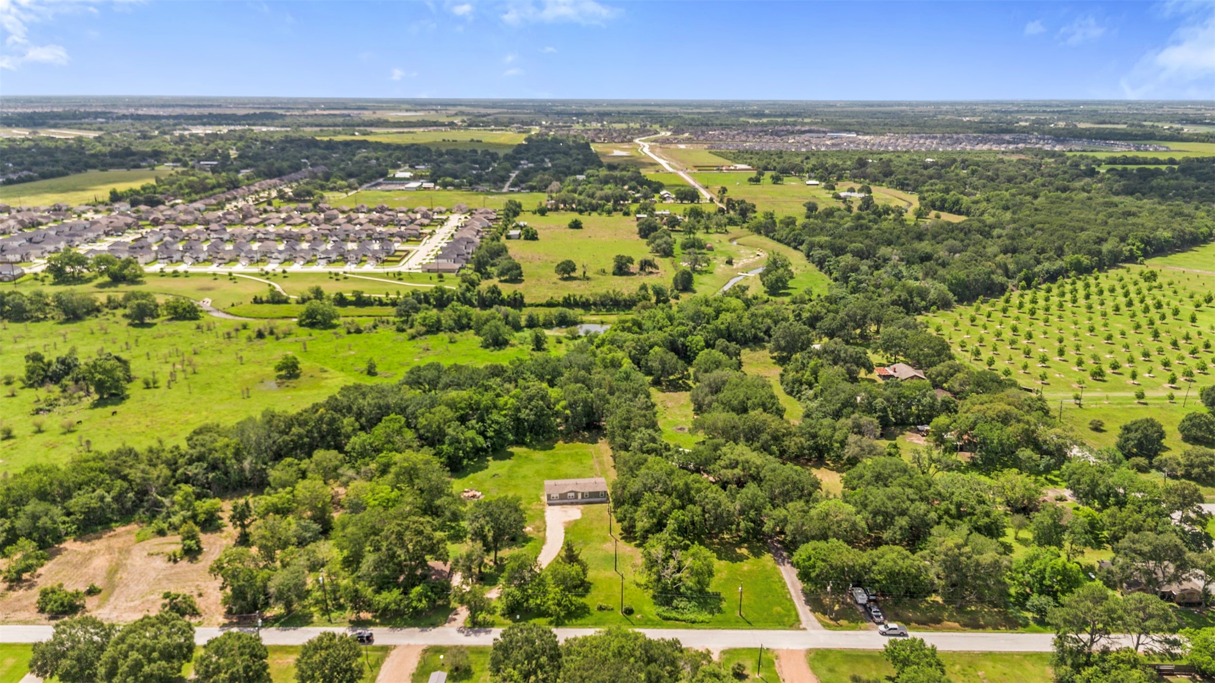 2701 Mazen Road Rosenberg, TX 77471 - Photo 7 of 10 This aerial photo showcases a spacious rural landscape with lush greenery, scattered trees, and a small house. Nearby, there's a residential neighborhood, offering a blend of country living with community access.