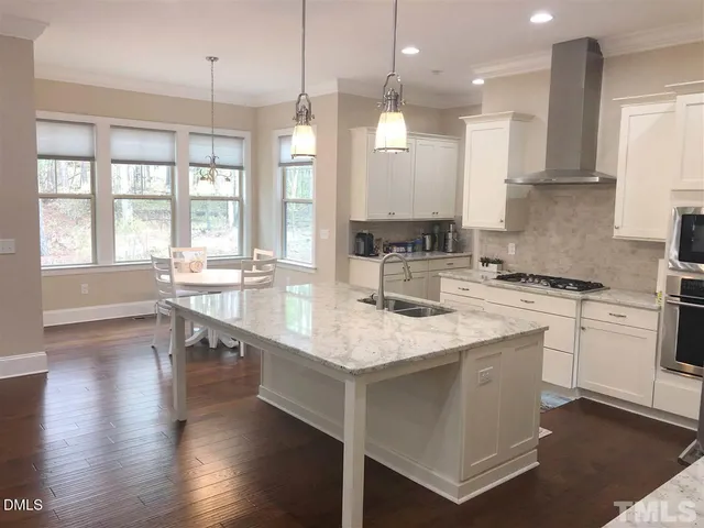 a kitchen with stainless steel appliances granite countertop a stove a sink a oven a dining table with white cabinets and wooden floor