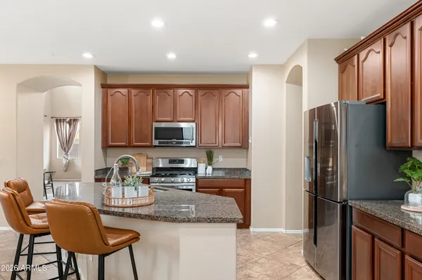 a kitchen with stainless steel appliances granite countertop a refrigerator a stove a sink a dining table and chairs with wooden floor