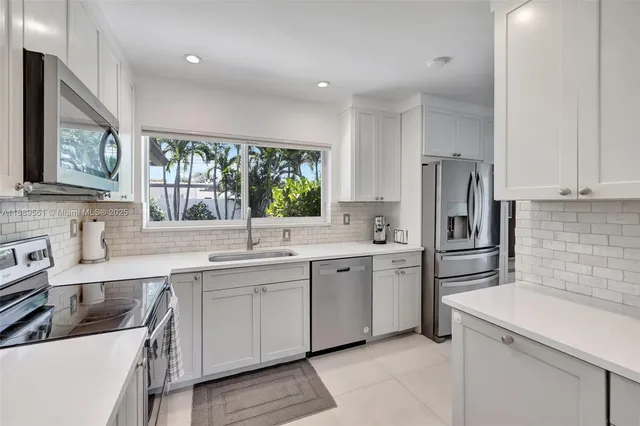 a large white kitchen with a window and stainless steel appliances