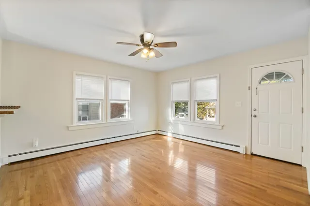 an empty room with wooden floor chandelier fan and windows