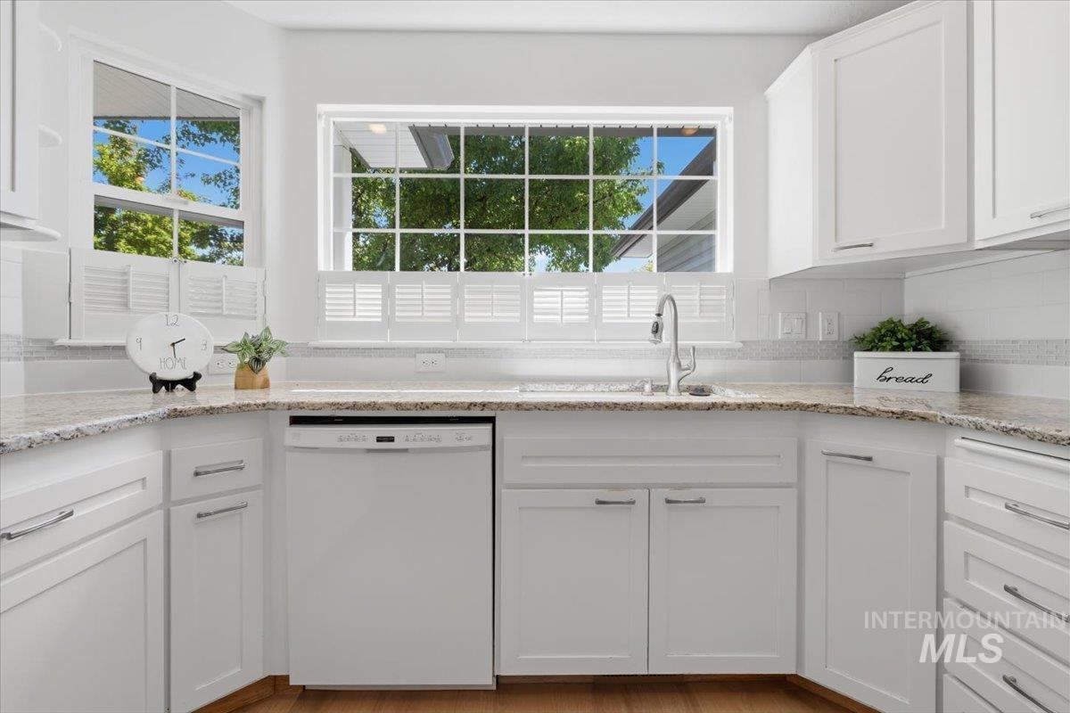 2075 North Springland Place Boise, ID 83713 - Photo 12 of 49 Bright kitchen featuring white cabinetry with brushed nickel hardware, granite-style countertops, a white tile backsplash, and wood-finish flooring