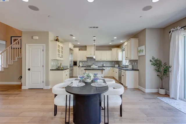 a kitchen with stainless steel appliances granite countertop a sink a refrigerator a stove a oven and white cabinets with wooden floor