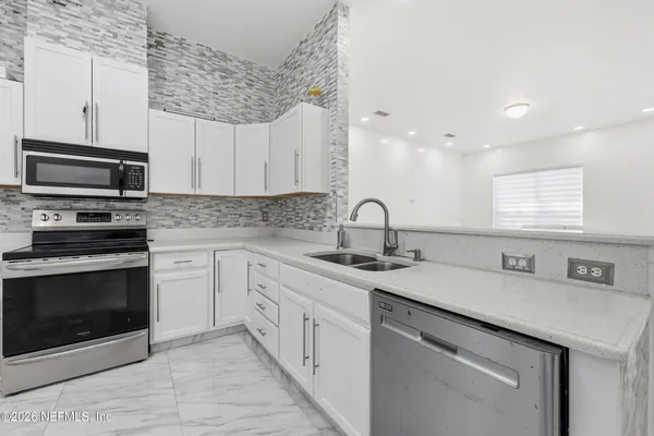 a kitchen with stainless steel appliances granite countertop a sink dishwasher a stove and a microwave oven with white cabinets