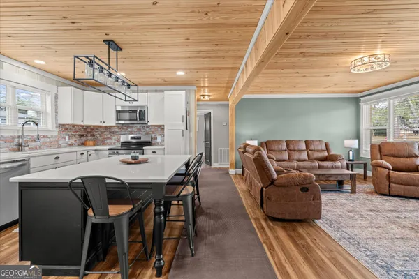 a living room with stainless steel appliances furniture a chandelier open kitchen view