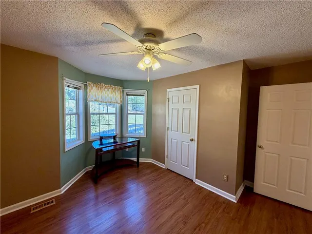 an empty room with wooden floor fan and windows