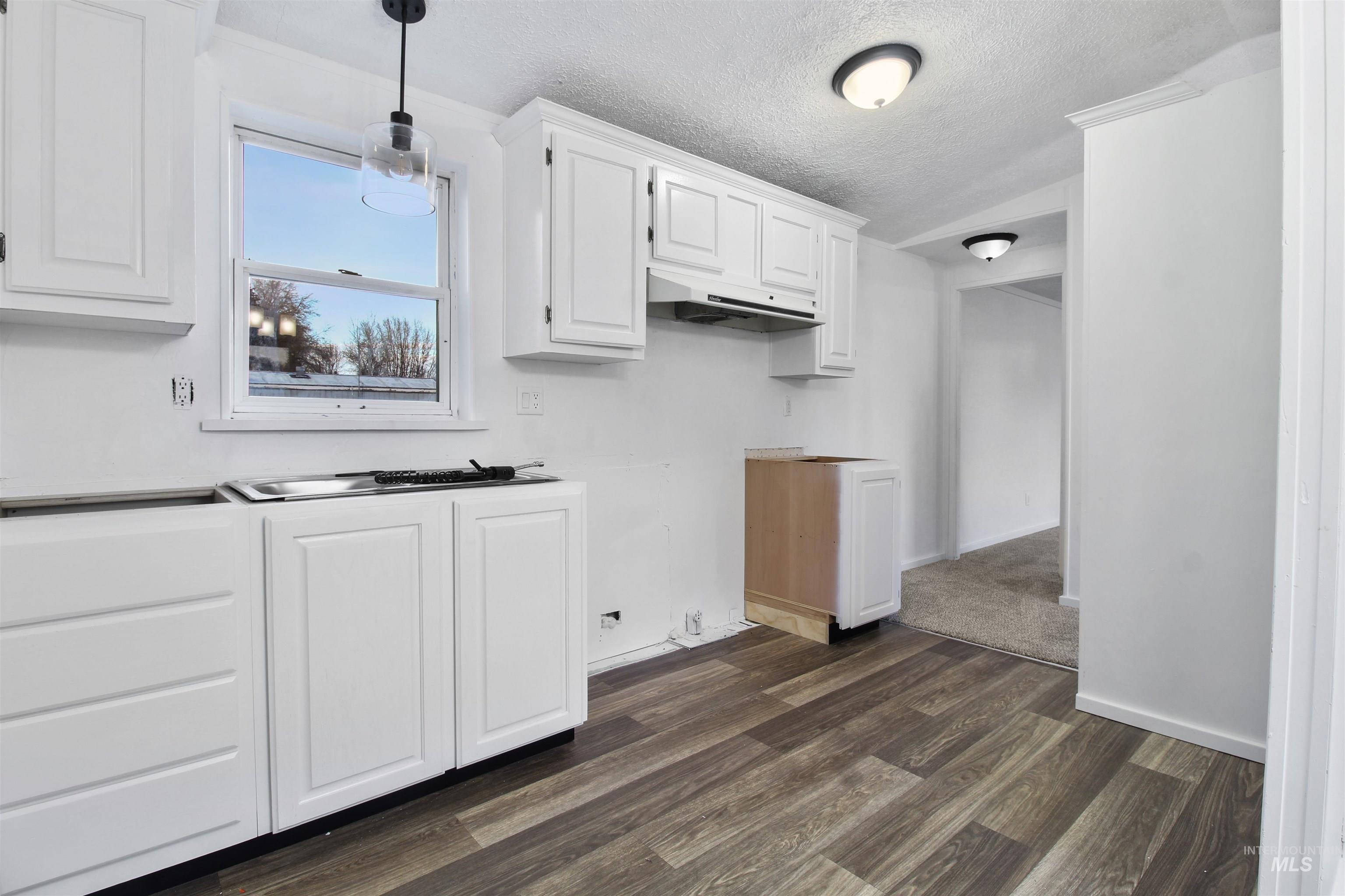377 South 200 West, Unit 36 Rupert, ID 83350 - Photo 18 of 31 Kitchen with white cabinets, dark wood finished floors, a textured ceiling, pendant lighting, and under cabinet range hood