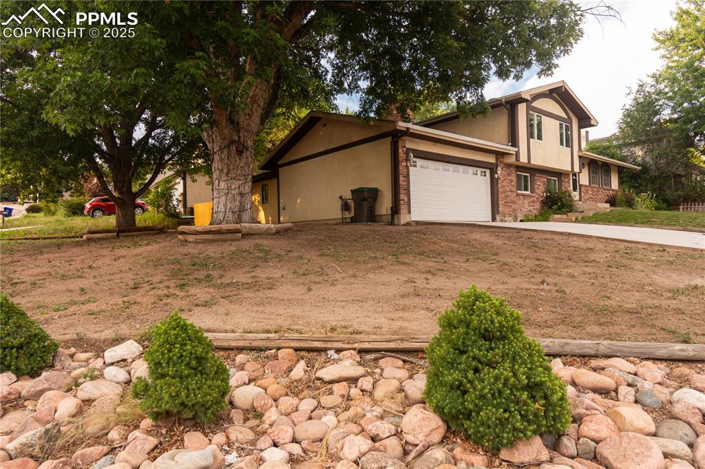 View of side of home with concrete driveway, stucco siding, brick siding, and an attached garage